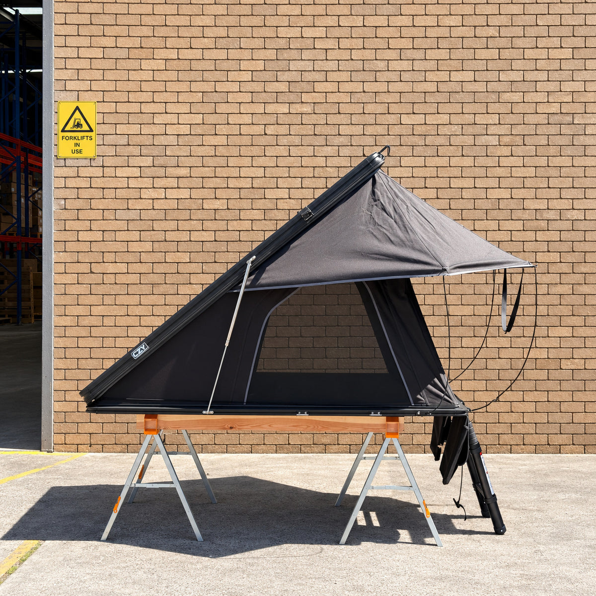 CZY AIR rooftop tent side profile on the original ToughBuilt sawhorses and timber frame outside a clean brick warehouse.