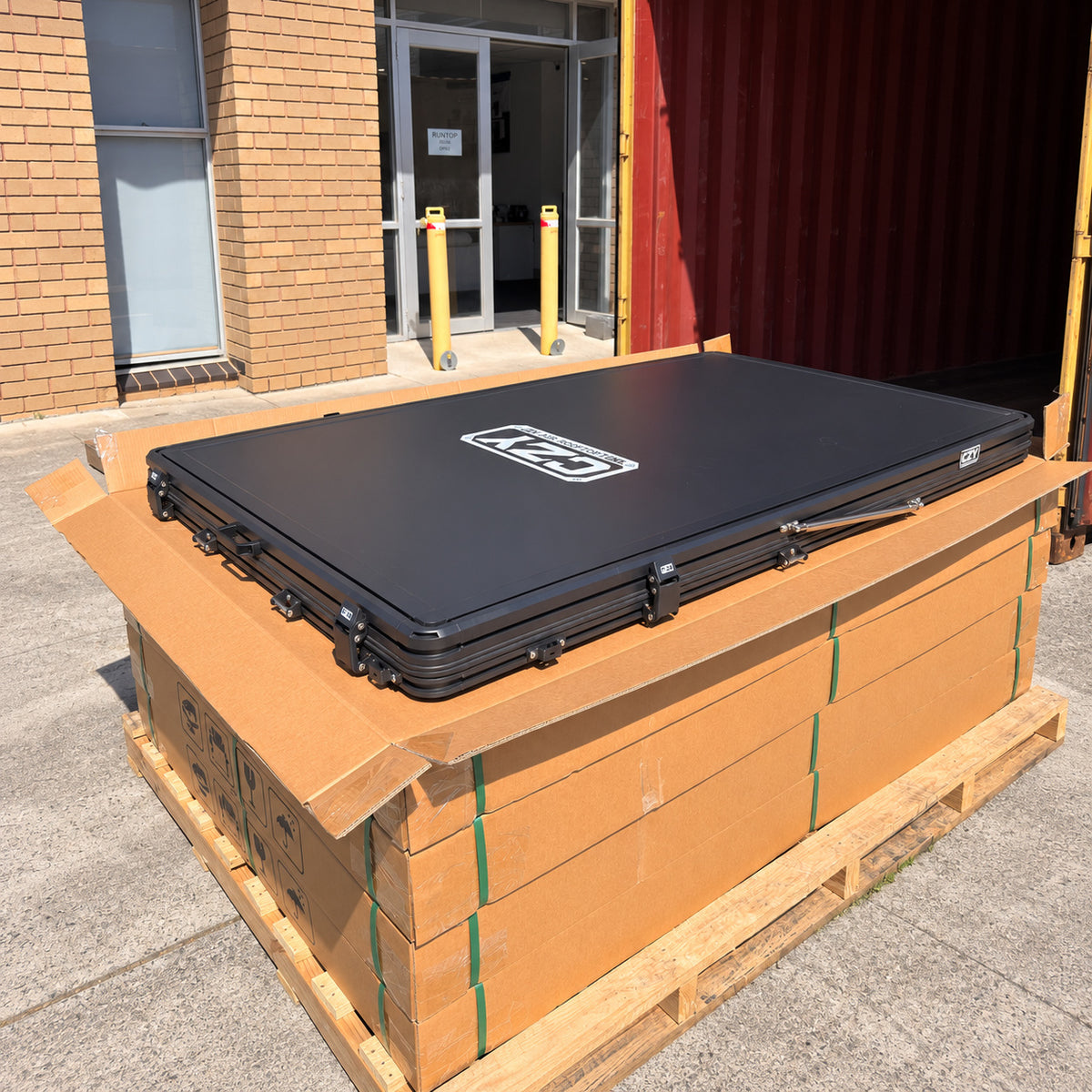 Closed CZY AIR rooftop tent resting on its original cardboard carton display outside the warehouse.