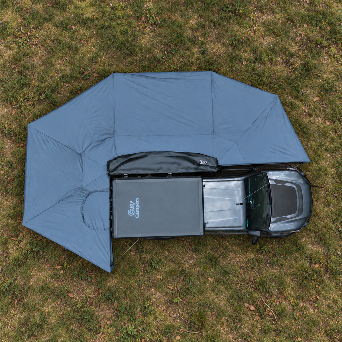Overhead view of the XL 270 Plus awning deployed beside a grey ute on grass, with the rooftop tent closed.