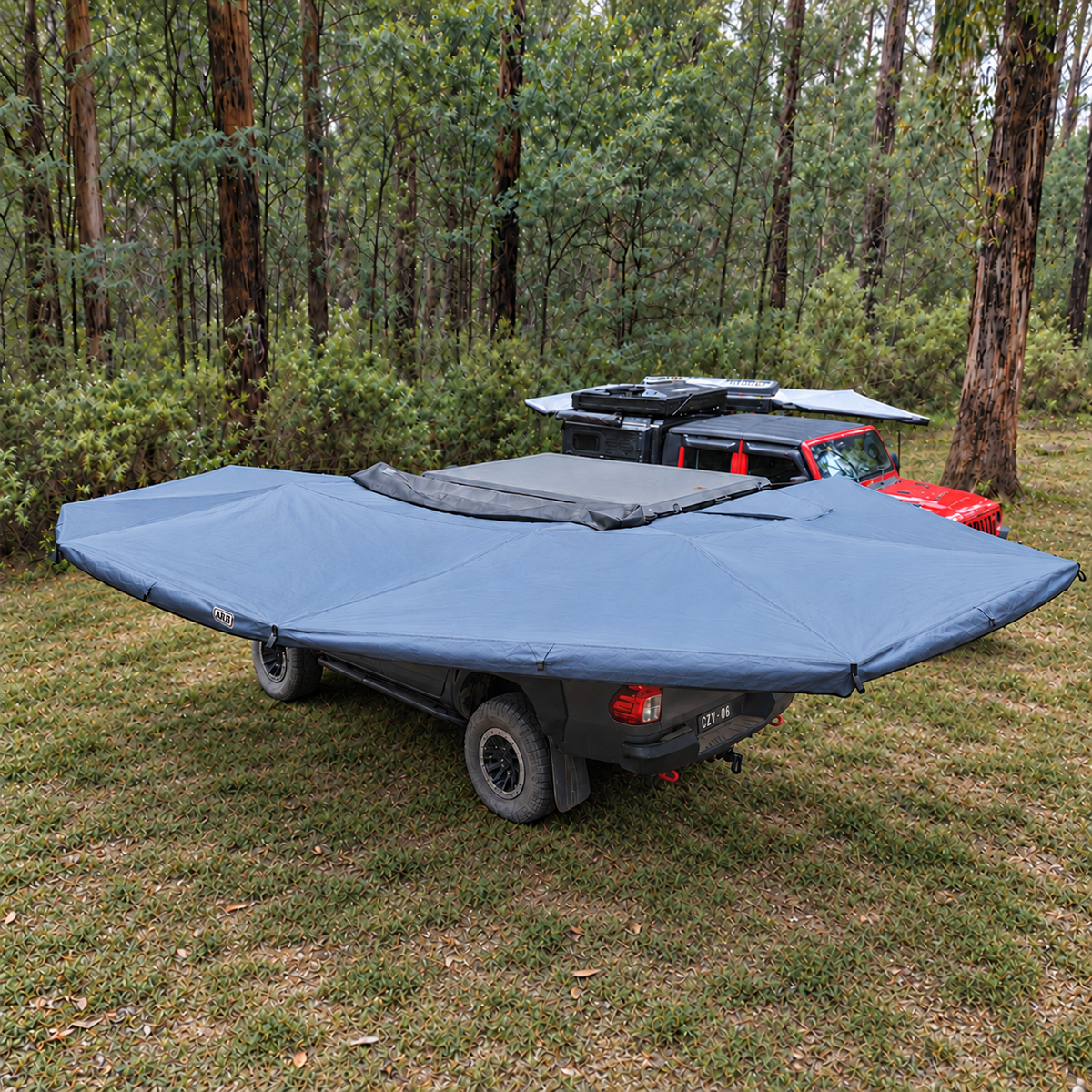 Side view of the XL 270 Plus awning deployed beside a grey ute on grass, with the rooftop tent closed.