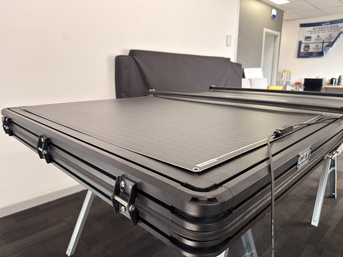 DOKIO 200W flexible solar panel on a closed rooftop tent, showing the low-profile panel and corner eyelet